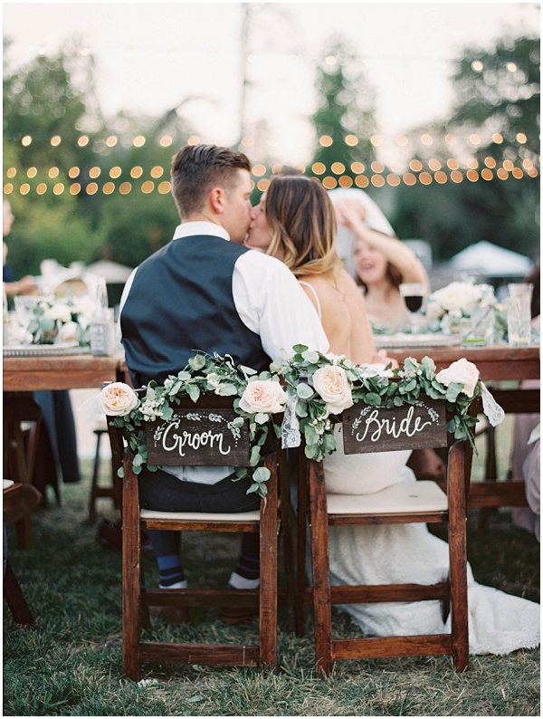 bride and groom kissing during wedding reception in "bride" and "groom" decorated chairs at Bridgewater Farm in Scotts Valley