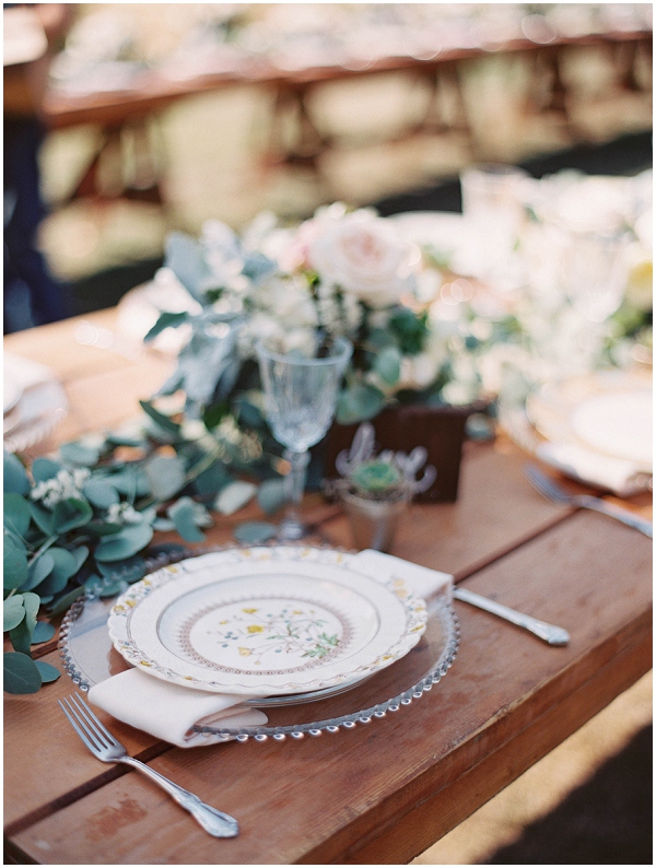 wedding reception table with beatuiful place setting and lush florals down center of wood table 