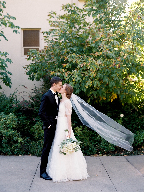 bride and groom kissing with wind swooping away veil