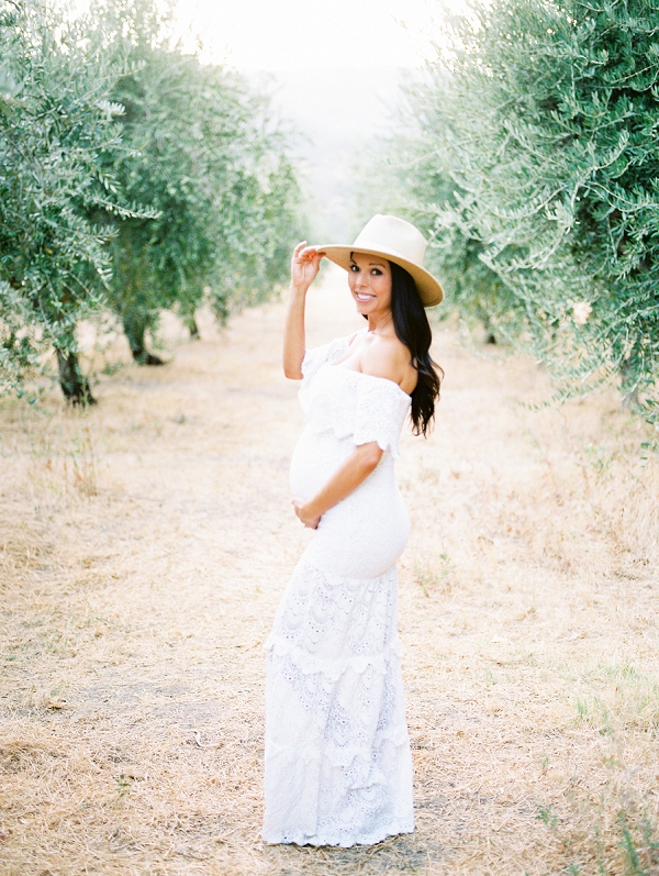 pregnant woman hlding hat in olive grove in napa