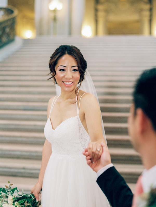 bride holding grooms hand on the staircase at San Francisco city hall.  