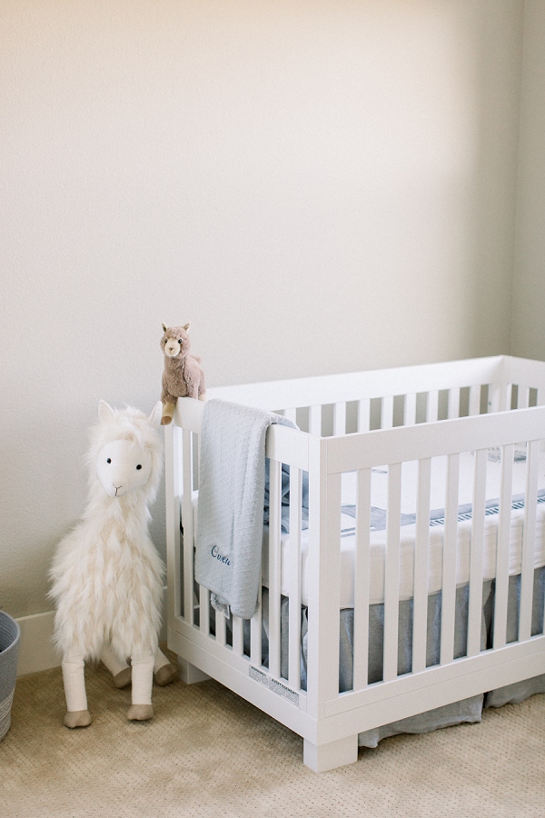 newborn photography showcasing a nursery with a stuffed llama, neutral walls, and a white crib