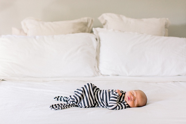 newborn photography session with a newborn sleeping on its tummy in a striped onesie laying on a freshly made bed