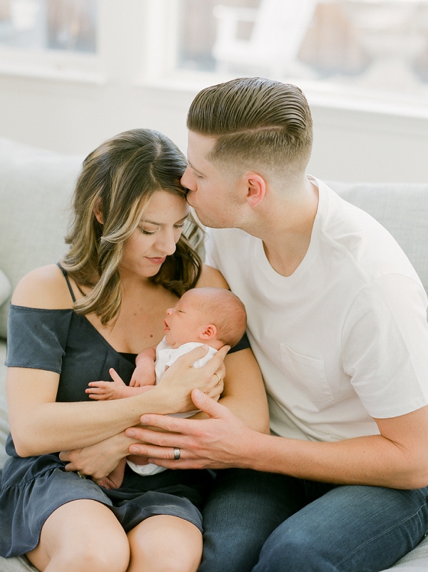 newborn photography session in San Francisco where mom is looking down at baby in her arms and dad is kissing her head.