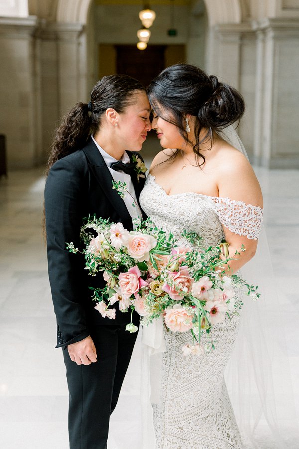 Brides with their heads together under the archway on the Fourth Floor Gallery at SF City hall for their elopement