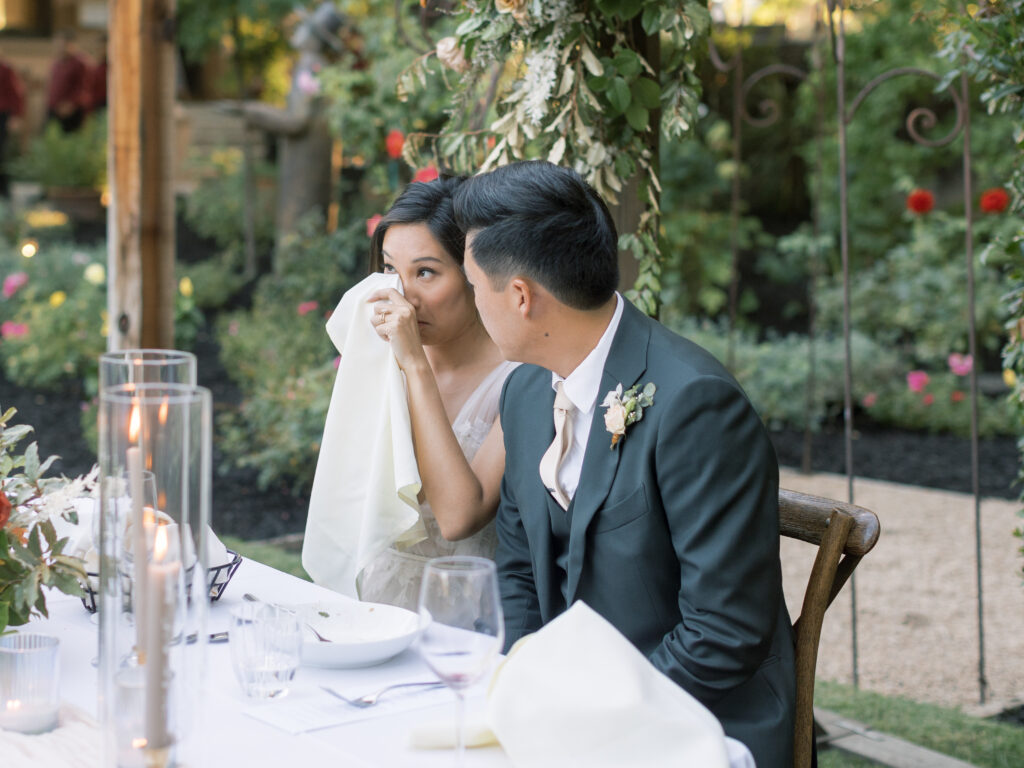 Bride blotting her tears and groom looking at her during toasts. Tres Posti Napa Valley Wedding