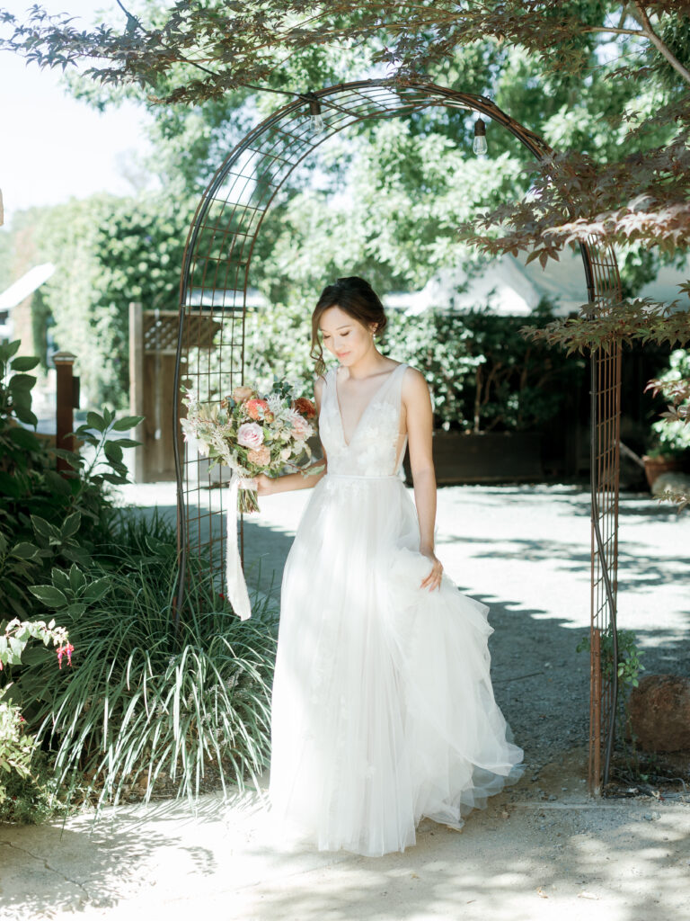 Brides walking down the pathway holding her bouquet. Tres Posti Napa Valley Wedding
