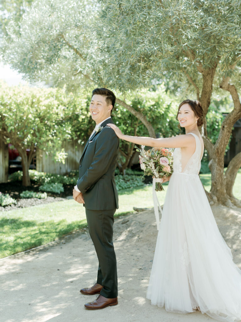 Groom smiling for first look and bride putting her hand on his shoulder. Tres Posti Napa Valley Wedding