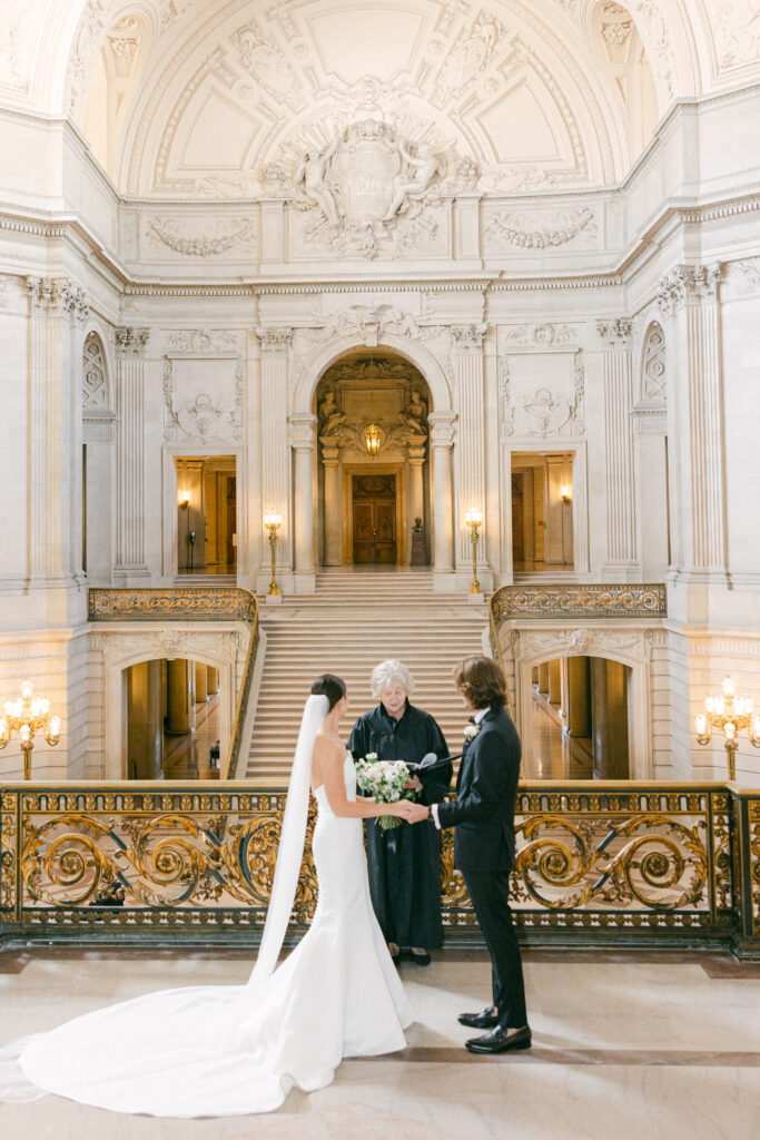 bride and groom exchanging vows at San Francisco City Hall with teh Grand Staircase behind them