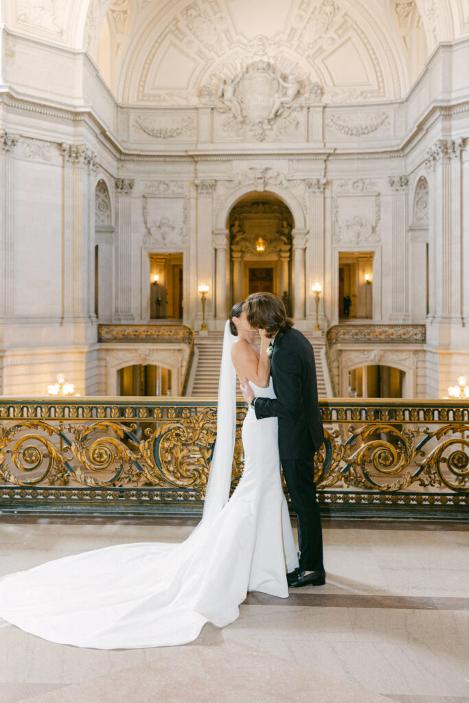 Bride and Groom kissing on the rotunda with the Grand Staircase behind them at San Francisco City Hall