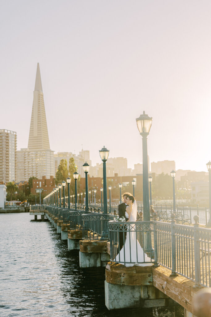 bride and groom on the boardwalk with san francisco city skyline behind them