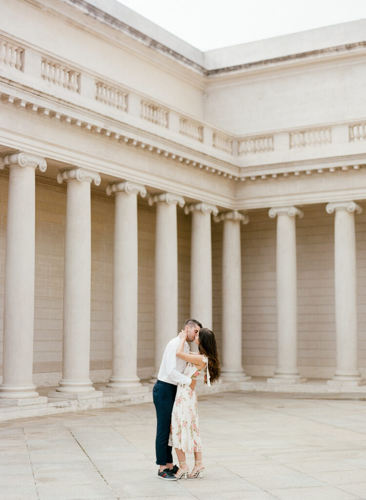 man and woman kissing at the Legion of Honor.  Pillars are surrounding them