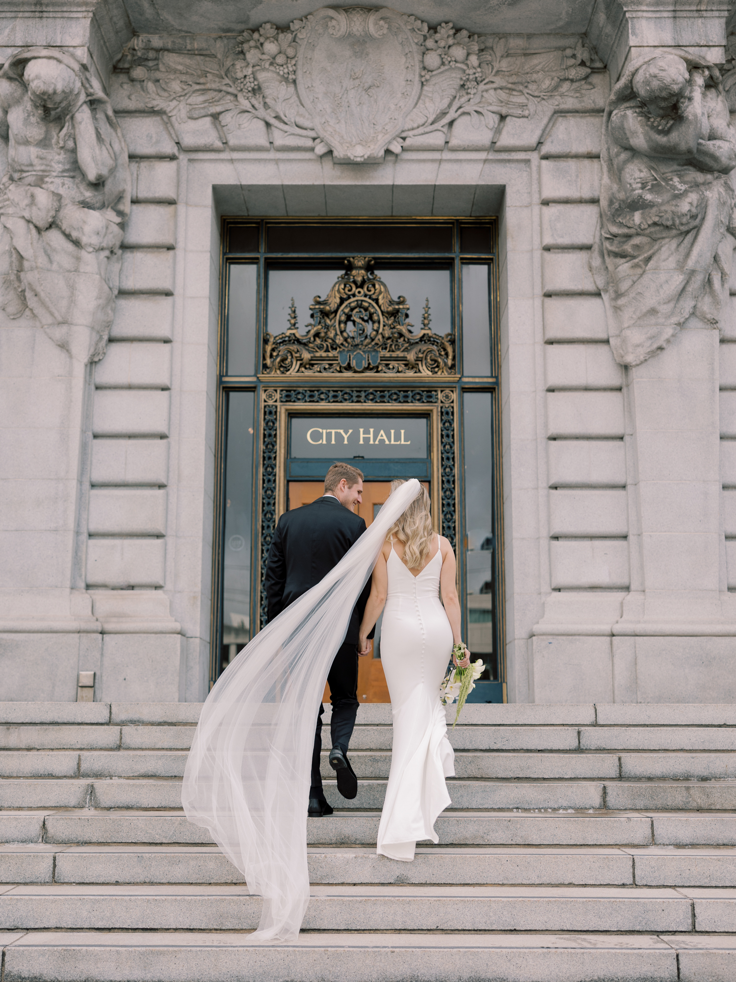 Bride walking into San Francisco City Hall with veil flowing during her wedding portrait session